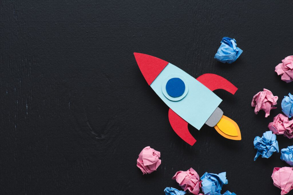 cardboard rocket with crumpled paper balls and copy space on black background, setting goals concept